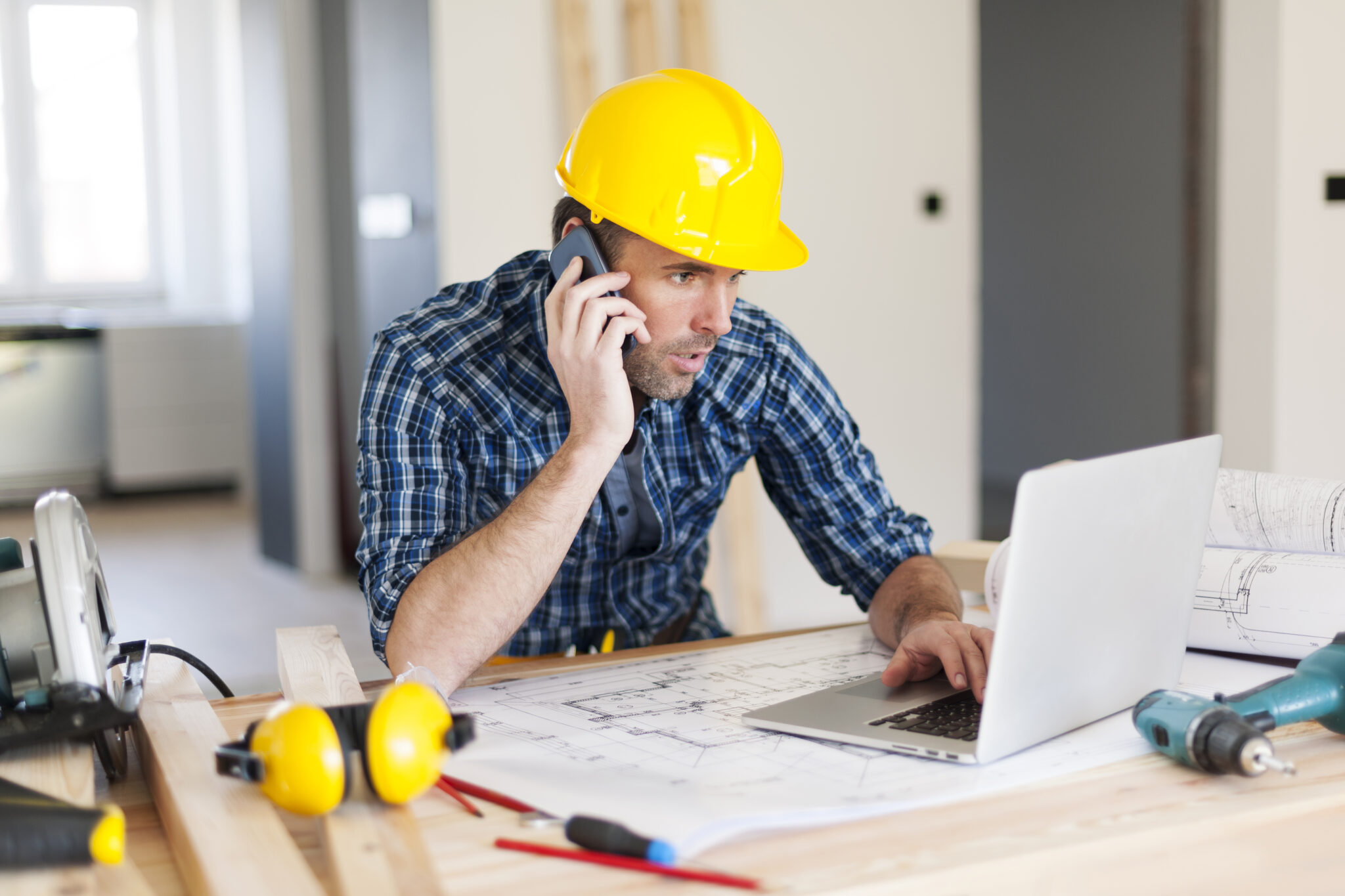 Man talking on mobile phone and using laptop on construction side